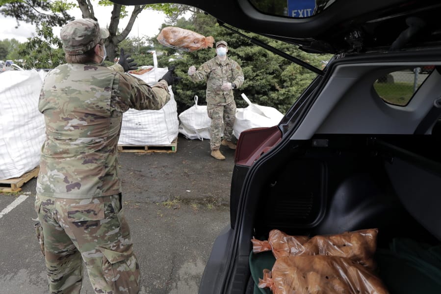 Members of the Washington National Guard toss a bag of potatoes as they load a waiting car, Thursday, May 14, 2020, during the free distribution of 200,000 pounds of potatoes provided by the Washington State Potato Commission in Tacoma, Wash. Most of the potatoes were donated by farmers across the state who have not been able to sell to their regular restaurant customers due to the coronavirus pandemic. (AP Photo/Ted S.