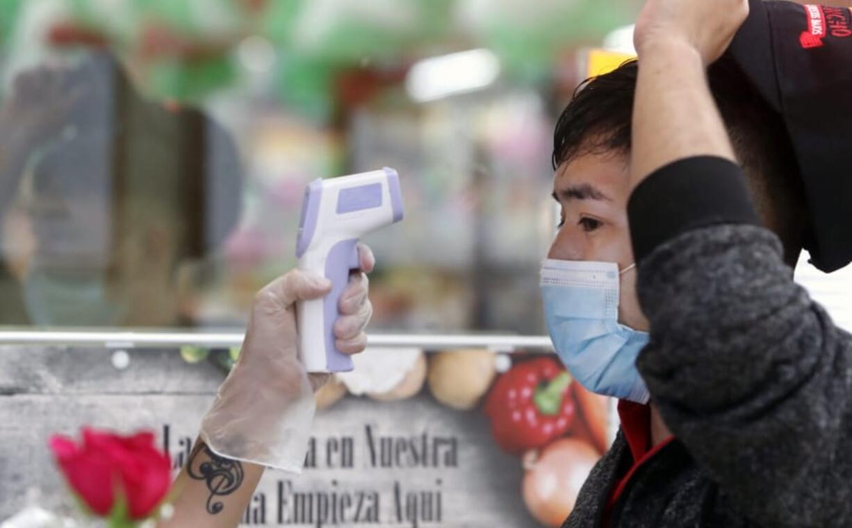 FILE - In this May 12, 2020 file photo, amid concerns of the spread of COVID-19, Ronaldo Santos has his temperature checked before starting his work shift in the meat department of a grocery store in Dallas. With more businesses across the country easing back to life, the new challenge will be how to keep workers safe during the pandemic. From temperature checks, contact tracing, social distancing and staggered schedules, a variety of new protocols are being implemented.