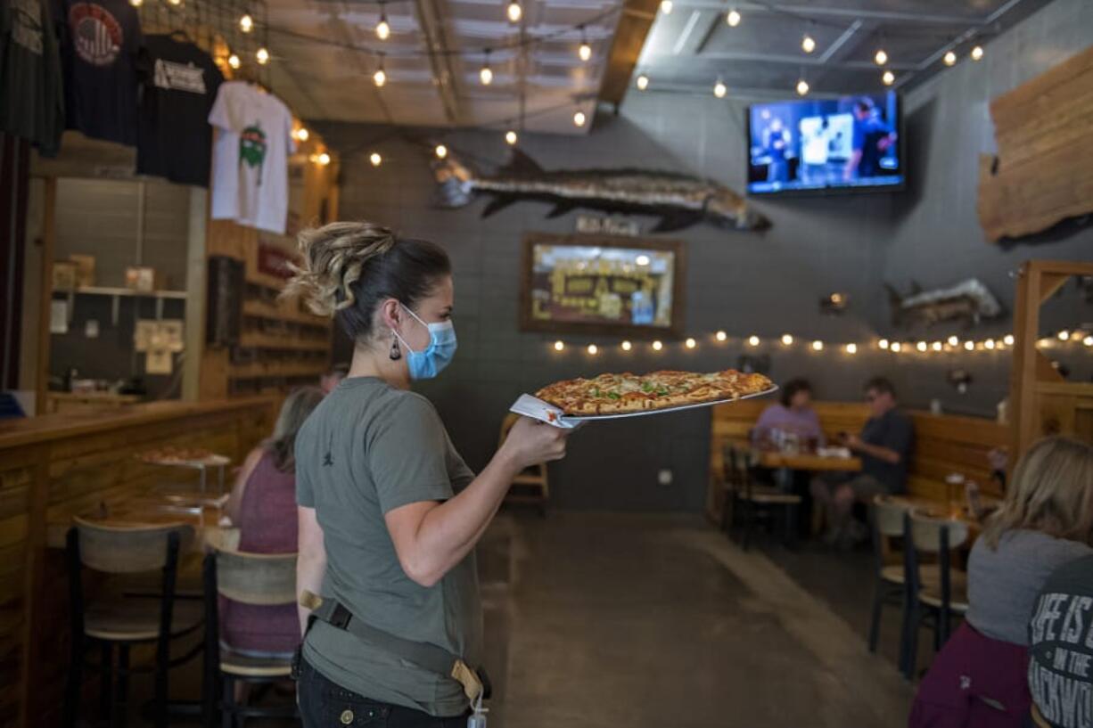 Crystal Badley of Backwoods Brewing Company wears a protective mask as she serves a fresh pizza to customers in Carson on Thursday afternoon. Carson, which is located in Skamania County, is already in Phase 2 of the reopening plan outline by Gov. Jay Inslee during the COVID-19 pandemic.