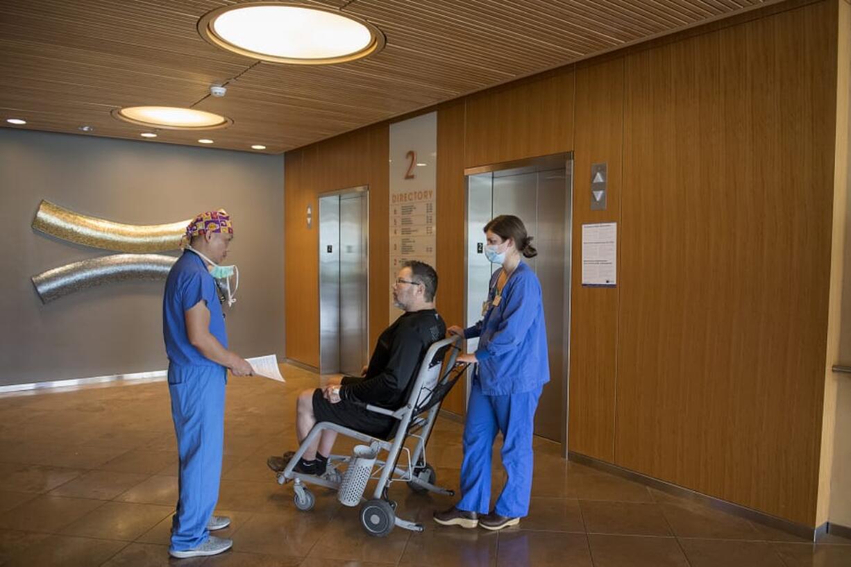 Dr. Nelson Saldua, from left, talks with his patient, Scott Poverud of Vancouver, as he is wheeled out of the hospital by registered nurse Katie Yochim-Smith after having surgery at Legacy Salmon Creek Medical Center in Vancouver. Saldua said it was tough for him to take a break from surgery during the pandemic because his patients needed care.