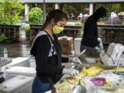 Kolby Wolfe, left, and Adolfo Santos whip up Gyros at the Greek Gyros booth at the Vancouver Farmers Market on Saturday. The market was initially limited to grocery vendors this year, but the lineup has gradually expanded to include hot food vendors.