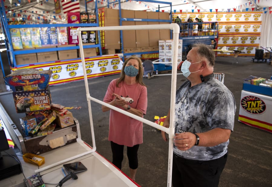 Cashier manager Charlotte Brown, left, and general manager Beau Leach describe the sneeze guards that will be set up at each register to protect employees at TNT Fireworks Warehouse in Hazel Dell. Leach said he went above the standard safety requirements and put extra steps in place to keep employees and customers safe. He ordered masks for customers to use for free if they do not have their own, as well as touchless hand sanitizer dispensers to place around the store.