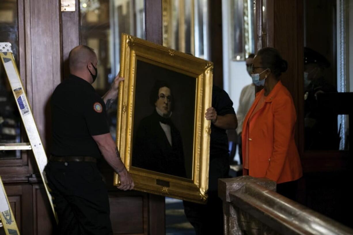 Clerk of the House Cheryl Johnson, right, watches as Architect of the Capitol maintenance workers remove a portrait of  Howell Cobb of Georgia that was hanging in the Speakers Lobby on Capitol Hill, Thursday, June 18, 2020, in Washington.