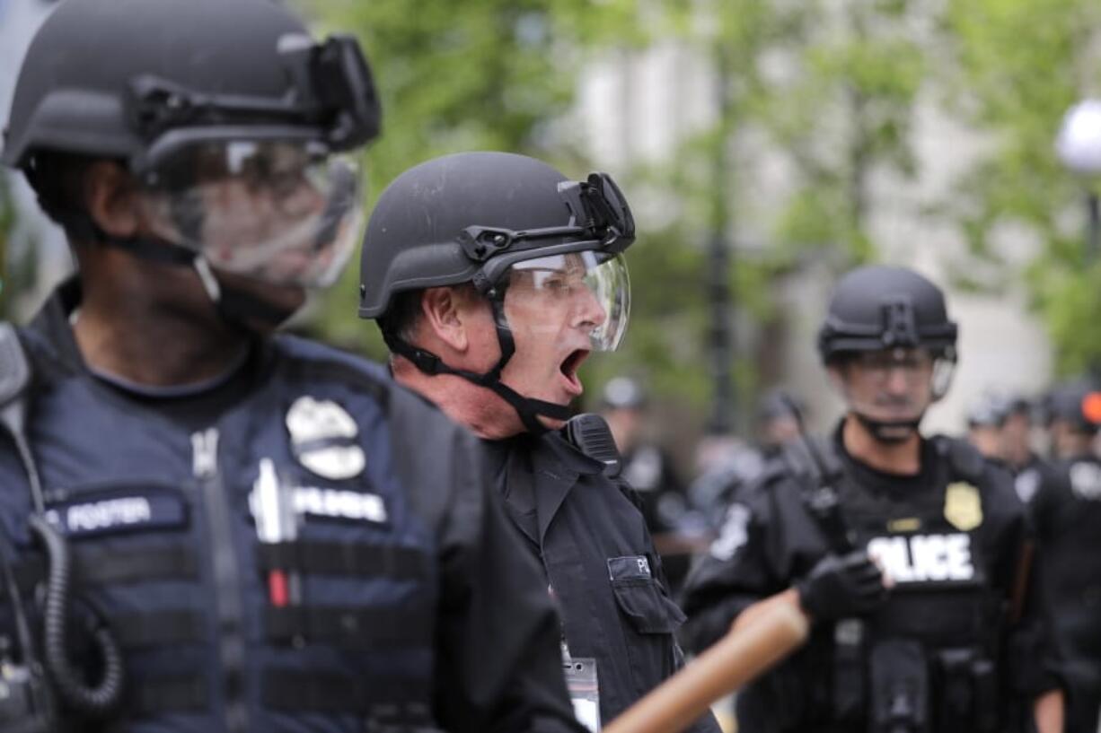 A Seattle police officer yells out orders at Seattle City Hall as protesters march toward them Wednesday, June 3, 2020, in Seattle, following protests over the death of George Floyd, a black man who died in police custody in Minneapolis.