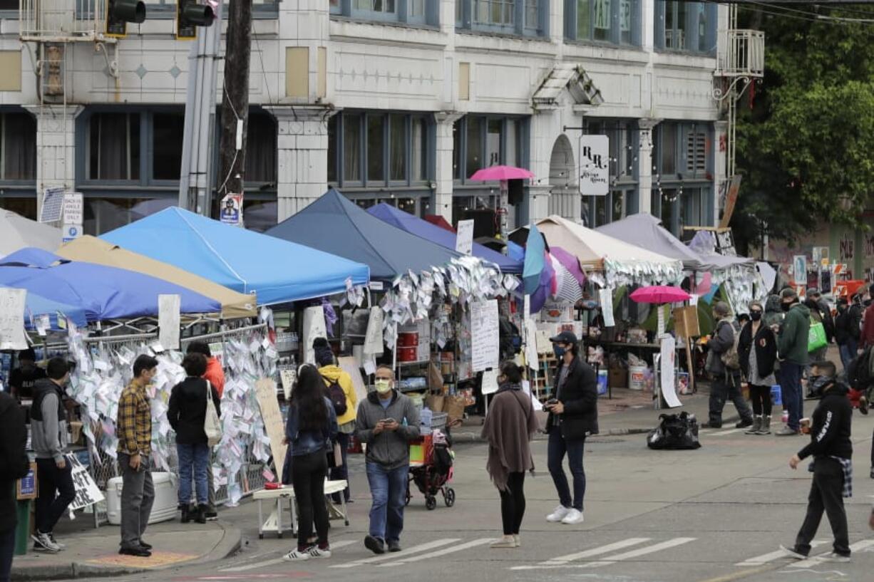 People walk near tents that make up the &quot;No Cop Co-op,&quot; Monday, June 15, 2020, inside what has been named the Capitol Hill Occupied Protest zone in Seattle. Protesters have taken over several blocks near downtown Seattle after officers withdrew from a police station in the area following violent confrontations. (AP Photo/Ted S.