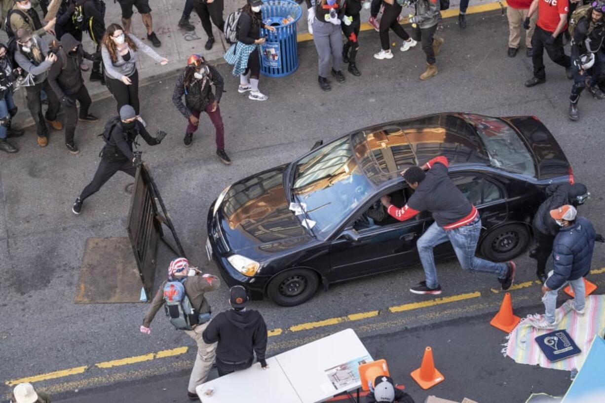 A man drives into the crowd at 11th and Pike, injuring at least one person, before exiting the car and brandishing an apparent firearm, Sunday, June 7, 2020, in Seattle, during protests over the death of George Floyd in Minneapolis. The man reaching into the car to stop it was injured.