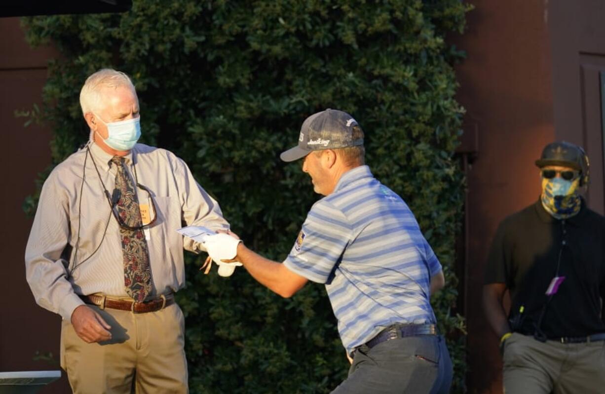 A rules official hands a score card to Ryan Palmer at the first tee during the first round of the Charles Schwab Challenge golf tournament at the Colonial Country Club in Fort Worth, Texas, Thursday, June 11, 2020. (AP Photo/David J.