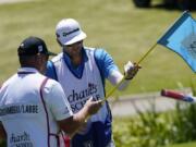 Dustin Johnson's caddie Austin Johnson, right, wipes down a putting green flag pole with a disinfectant wipe along with Bryson DeChambeau's caddie Tim Tucker during the first round of the Charles Schwab Challenge golf tournament at the Colonial Country Club in Fort Worth, Texas, Thursday, June 11, 2020. (AP Photo/David J.