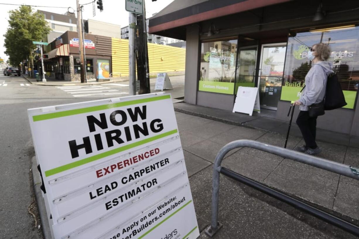 In this photo taken Thursday, June 4, 2020, a pedestrian wearing a mask walks past reader board advertising a job opening for a remodeling company, in Seattle. The U.S. unemployment rate fell to 13.3% in May, and 2.5 million jobs were added -- a surprisingly positive reading in the midst of a recession that has paralyzed the economy and depressed the job market in the wake of the viral pandemic.