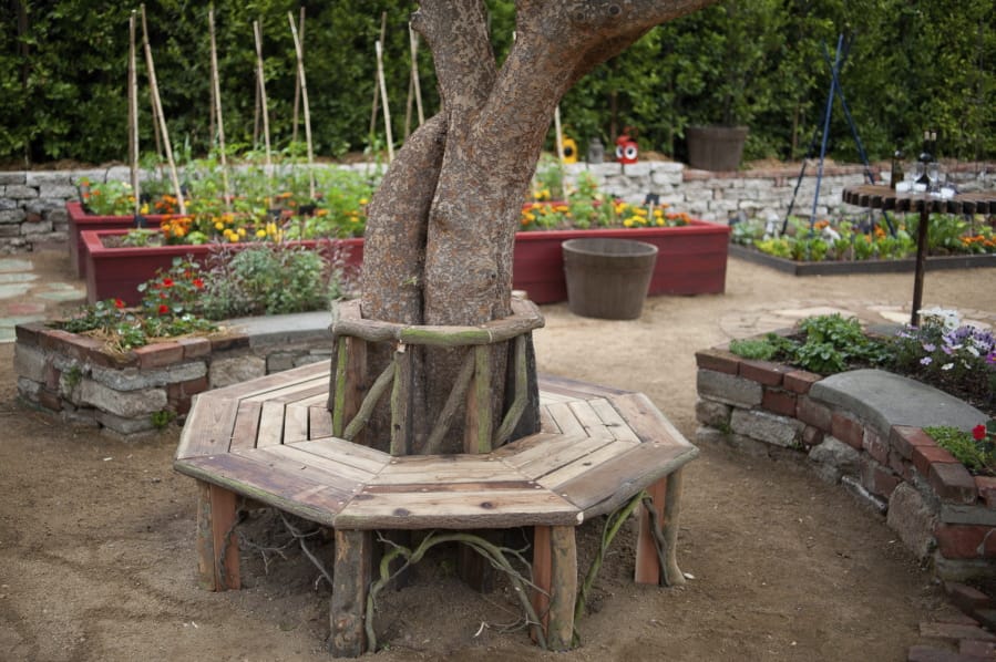 A bench around a tree and raised flower and vegetable beds.