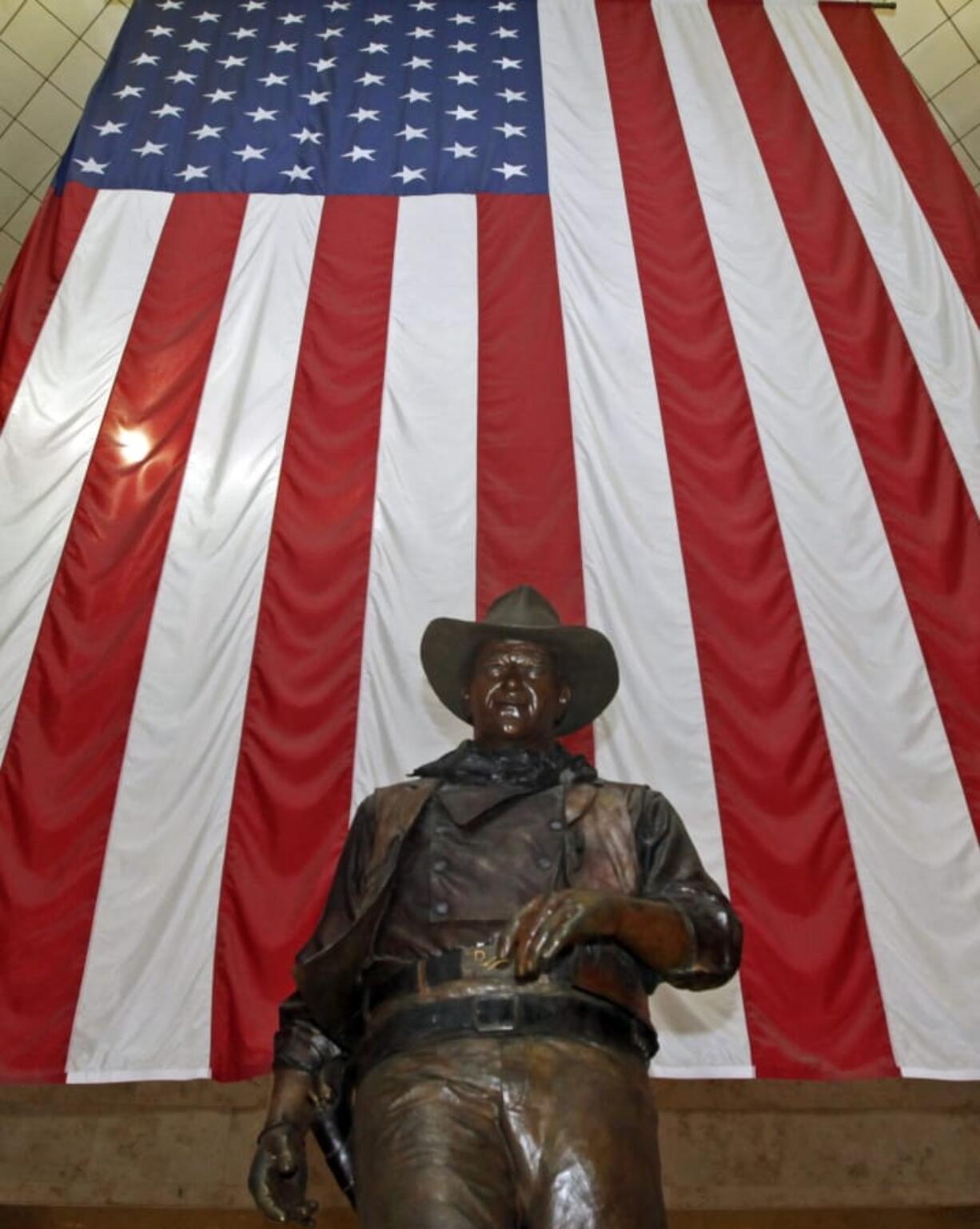 FILE - In this Sept. 11, 2011, file photo, a bronze statue of late actor John Wayne stands before a four-story high United States flag at John Wayne Orange County Airport in Santa Ana, Calif. In the latest move to change place names in light of U.S. racial history, leaders of Orange County&#039;s Democratic Party are pushing to drop film legend Wayne&#039;s name, statue and other likenesses from the county&#039;s airport because of his racist and bigoted comments.