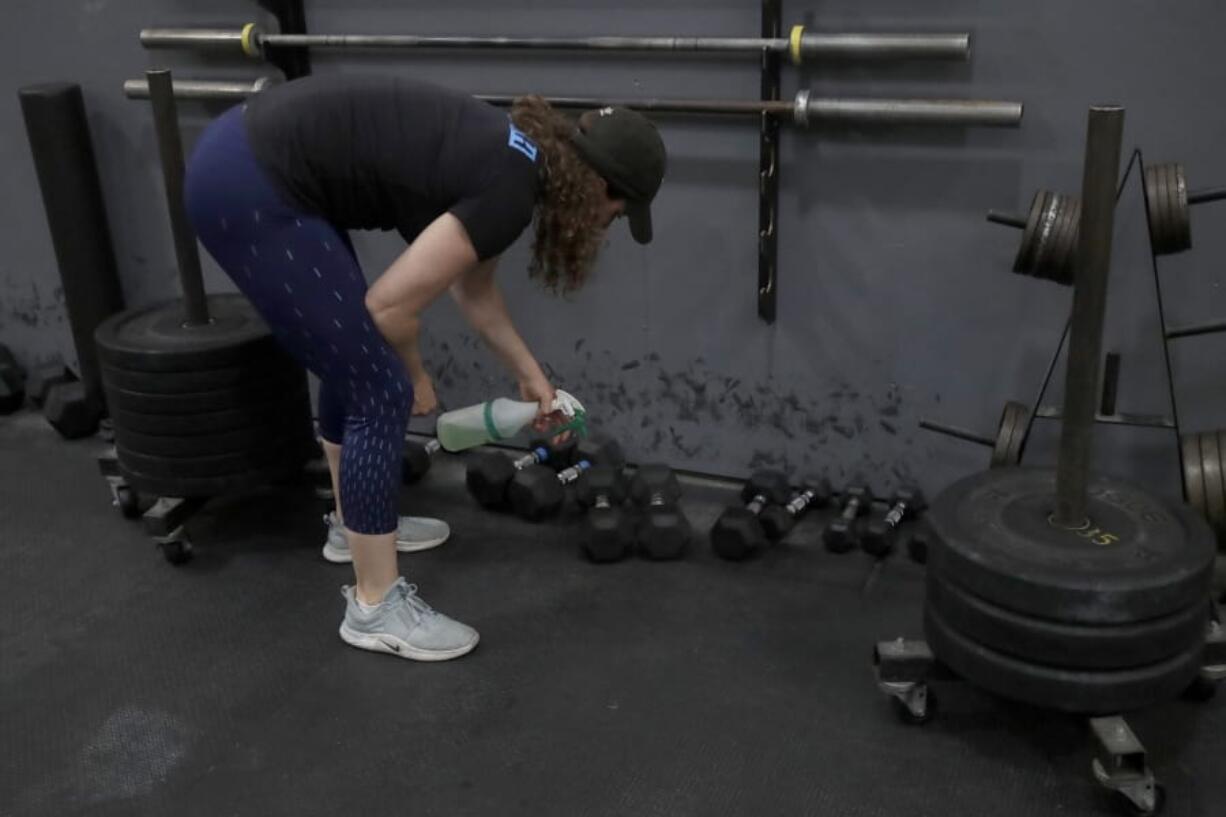 FILE - In a  Friday, April 24, 2020 file photo, Alexis Garrod, CrossFit Potrero Hill partner and head coach, cleans off weight training equipment in an empty gym, which closed for shelter in place orders over COVID-19 concerns, in San Francisco. Reebok says it has cut ties with CrossFit chief executive and founder invoked George Floyd&#039;s name in a Twitter post chastising a health group for saying that racism was a public health problem.