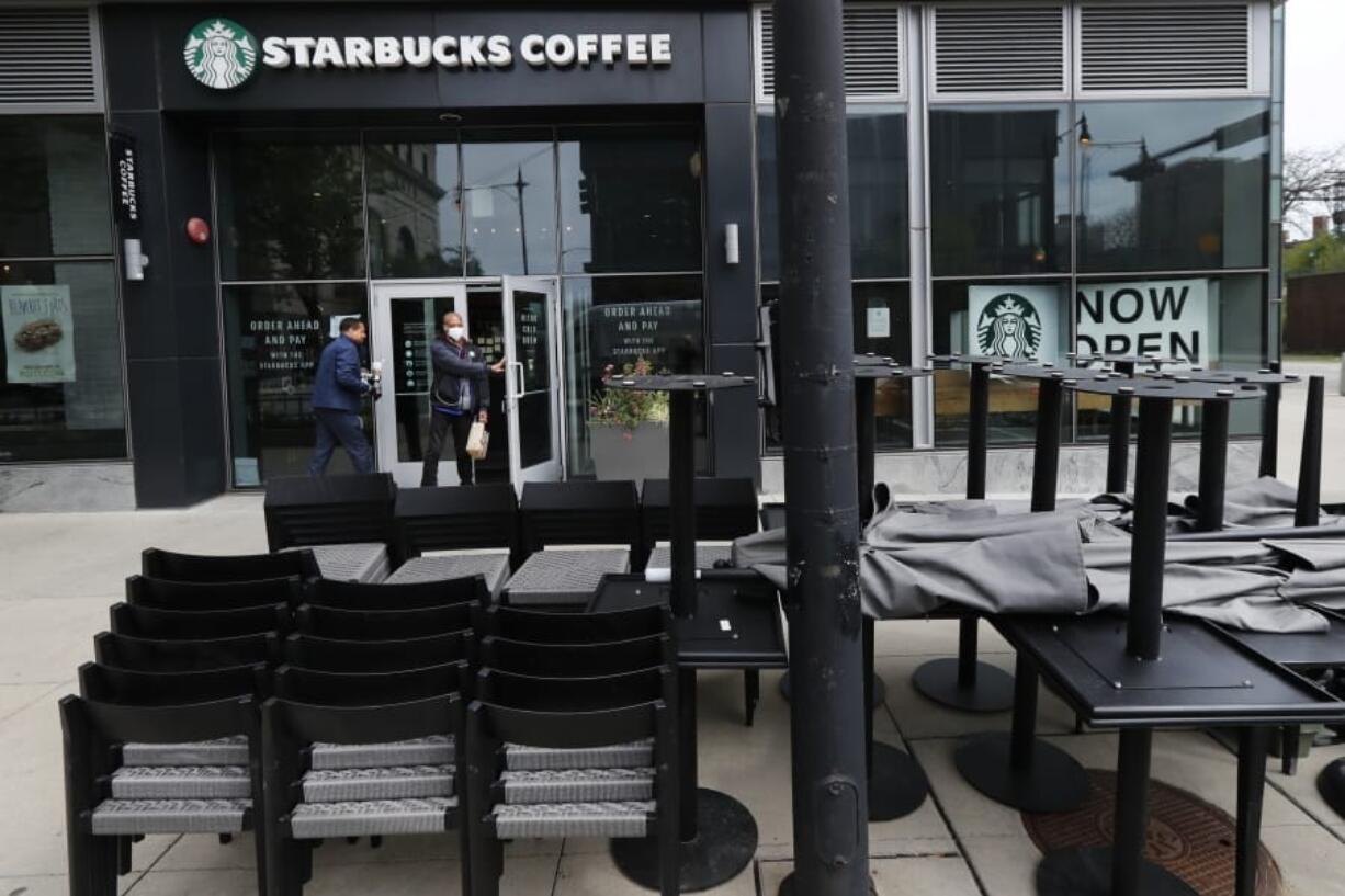 FILE - In this May 21, 2020 file photo, patrons to a Starbucks in the Chicago neighborhood of Hyde Park walk past stacked chairs and tables.  Starbucks says that the COVID-19 pandemic caused an approximately $3 billion to $3.2 billion decline in its third-quarter consolidated revenue. The coffee chain said Wednesday, June 10,  that the virus outbreak also lowered operating income by about $2 billion to $2.2. billion.