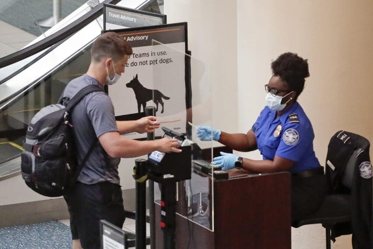 FILE - In this June 17, 2020 file photo, a TSA worker, right, checks a passenger before entering a security screening at Orlando International Airport  in Orlando, Fla.   A high-ranking Transportation Security Administration official says the agency is falling short when it comes to protecting airport screeners and the public from the new coronavirus, according to published reports. A federal office that handles whistleblower complaints has ordered an investigation.