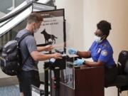 FILE - In this June 17, 2020 file photo, a TSA worker, right, checks a passenger before entering a security screening at Orlando International Airport  in Orlando, Fla.   A high-ranking Transportation Security Administration official says the agency is falling short when it comes to protecting airport screeners and the public from the new coronavirus, according to published reports. A federal office that handles whistleblower complaints has ordered an investigation.