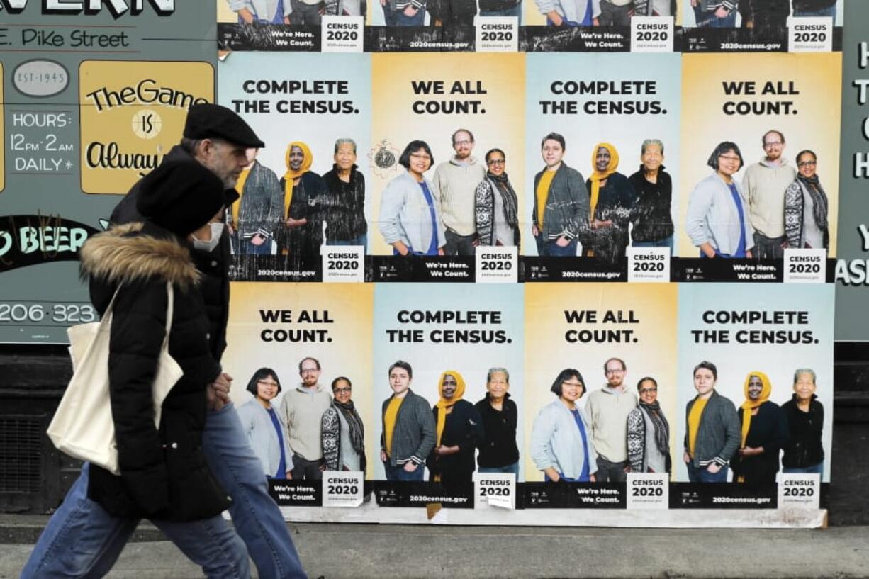 FILE - In this April 1, 2020, file photo, people walk past posters encouraging participation in the 2020 Census in Seattle&#039;s Capitol Hill neighborhood. Just how badly has the new coronavirus impacted life in the U.S.? The U.S. Census Bureau, along with five other federal agencies, will try to answer that question with a new experimental, weekly survey that just got approved earlier this week.  (AP Photo/Ted S.