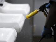 FILE - In this Thursday, March 19, 2020, file photo, a public school employee sanitizes a sink in a bathroom at a U.S. high school. Jobs with state and city governments are usually a source of stability in the U.S. economy, but the financial devastation wrought by the coronavirus pandemic has forced cuts that will reduce public services, from schools to trash pickup.