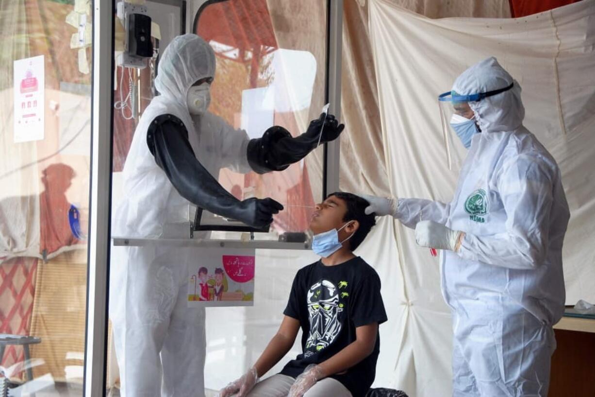 FILE - In this Friday, June 26, 2020 file photo, health workers take a nasal swab sample during a testing and screening operation for the new coronavirus, in Hyderabad, Pakistan.