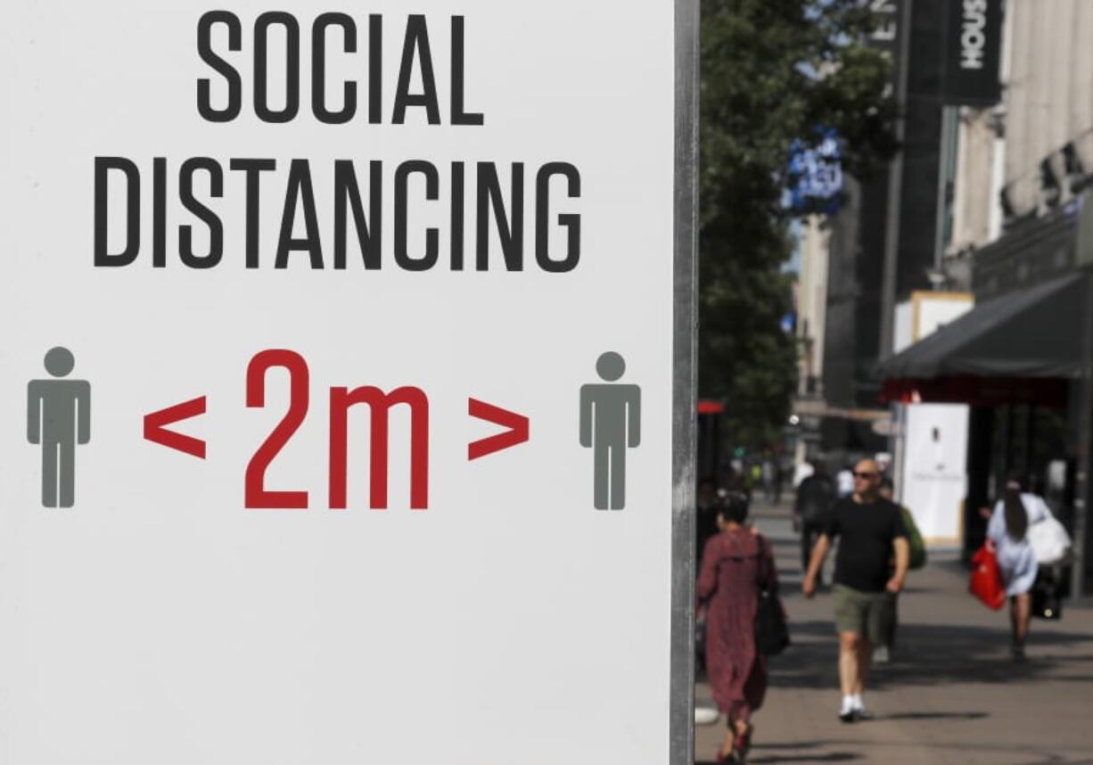 Shoppers pass a two meter social distance sign in London, Monday, June 22, 2020. The two-metre social distancing rule will be under review as the UK relax coronavirus lockdown measures implemented to stem the spread of the virus.