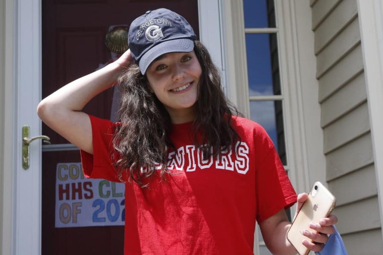 In this June 1, 2020 photo, high school graduate Lizzie Quinlivan wears a Georgetown University cap at her home in Hingham, Mass. Quinlivan has opted to attend closer-to-home Georgetown instead of colleges on the west coast which were on her original wish-list. As students make college plans for this fall, some U.S. universities are seeing surging interest from in-state students looking to stay closer to home amid the coronavirus pandemic.