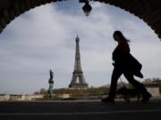 A woman walks her dog on a Paris bridge April 7, with the Eiffel Tower in background, during a nationwide confinement to counter the COVID-19.