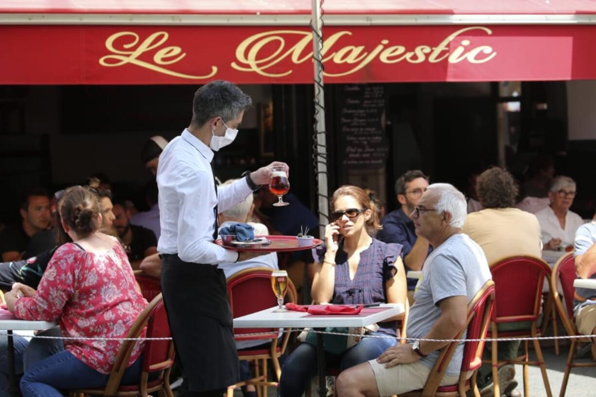 A bartender brings drinks to customers in a cafe of Saint Jean de Luz, southwestern France, Tuesday June 2, 2020. The French way of life resumes Tuesday with most virus-related restrictions easing as the country prepares for the summer holiday season amid the pandemic. Restaurants and cafes reopen Tuesday with a notable exception for the Paris region, the country&#039;s worst-affected by the virus, where many facilities will have to wait until June 22 to reopen.