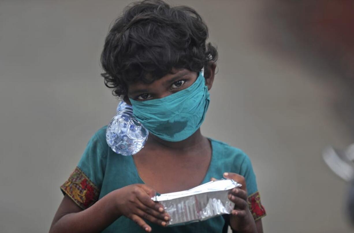 A girl wearing a face mask walks with a bottle of drinking water and a food packet that she received from a food distribution site in Mumbai, India, Saturday, June 20, 2020. India is the fourth hardest-hit country by the COVID-19 pandemic in the world after the U.S., Russia and Brazil.