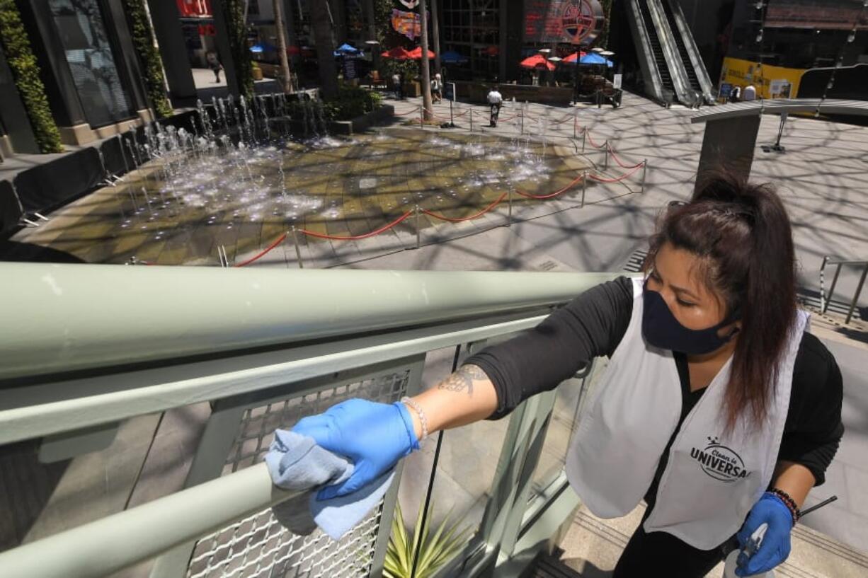 FILE - In this Thursday, June 11, 2020 file photo, Andrea Castaneda cleans the railings at Universal CityWalk near Universal City, Calif. On Friday, June 12, 2020, the Centers for Disease Control and Prevention posted guidelines to reduce the risk of COVID-19 coronavirus infection, along with a set of &quot;considerations&quot; for organizing and attending mass gatherings, as people emerge from stay-at-home lock downs and attempting some semblance of normal life. (AP Photo/Mark J.