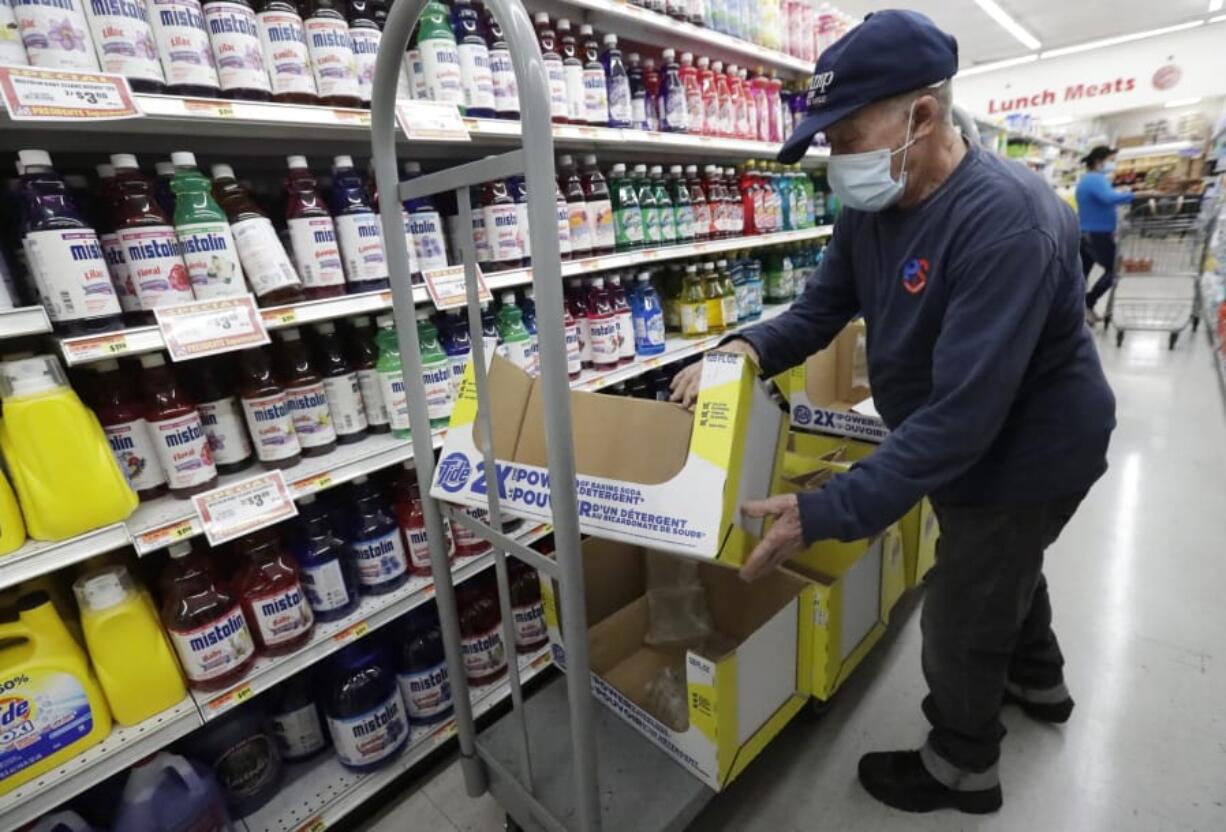 In this Wednesday, June 3, 2020 photo, Juan Santos stocks shelves at the Presidente Supermarket in the Little Havana neighborhood of Miami.  The U.S. government is set to issue its latest report on the layoffs that have left millions unemployed but have steadily slowed as many businesses have begun to reopen and to rehire some laid-off workers.