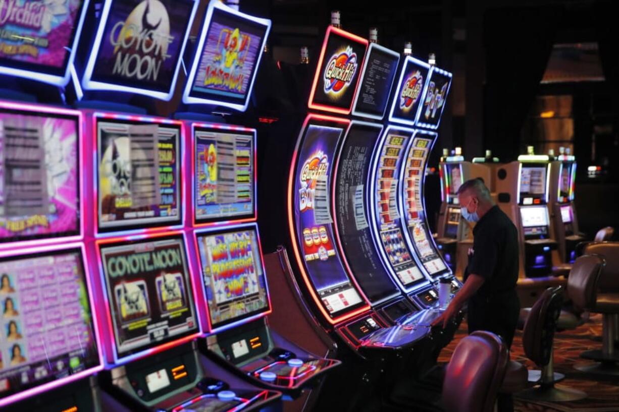 FILE - In this May 21, 2020, file photo, a worker looks over an electronic slot machine as chairs have been removed from some machines to maintain social distancing between players at a closed Caesars Palace hotel and casino in Las Vegas. Cards will be cut, dice will roll and jackpots jingle when casinos in Las Vegas and Nevada begin reopening at 12:01 a.m. Thursday, June 4. There will be big splashes, even amid ongoing unrest, and big hopes for recovery from an unprecedented and expensive closure prompted by the coronavirus pandemic.