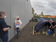 Patrick Quinlan, from left, and Linda Karschney of Living Hope Church chat with Mandi Holper as she settles in for the evening with her dog, Baby, at a temporary homeless encampment outside the church on May 5.