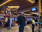 Security officer Stephen Henderson, center, wears a mask and gloves as he keeps an eye on the reopening while a thermometer, right, measures the temperature of guests at ilani. The casino says it has invested $1 million in safety measures, but workers have expressed concerns around enforcement.