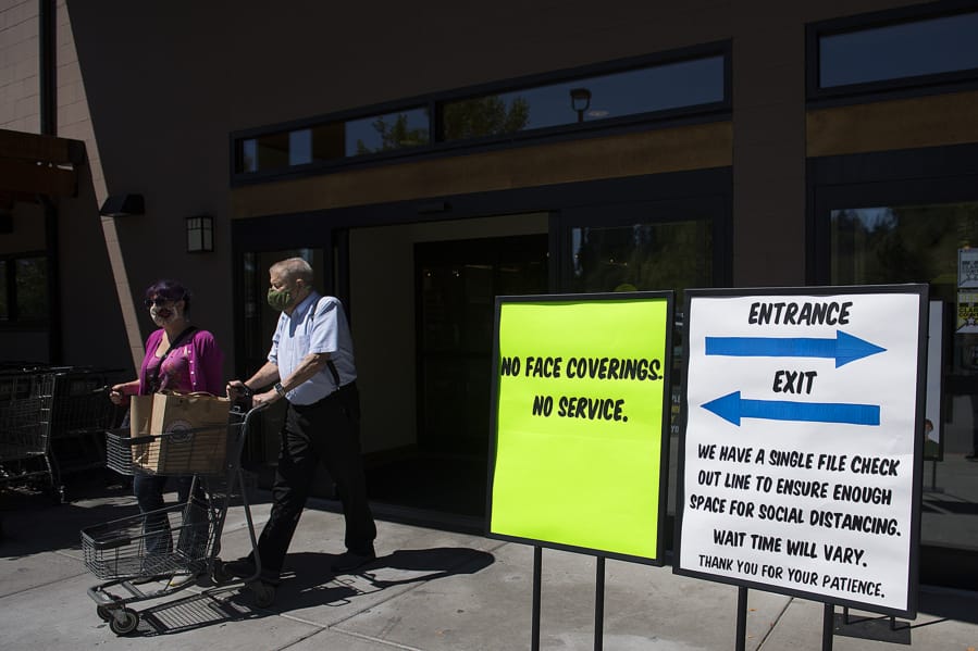 Kirsten Johnson of Vancouver, left, and her father, Ron, are in compliance with store and state policy while wearing protective face masks as they leave Chuck's Produce & Street Market in Salmon Creek with their groceries on Tuesday afternoon.