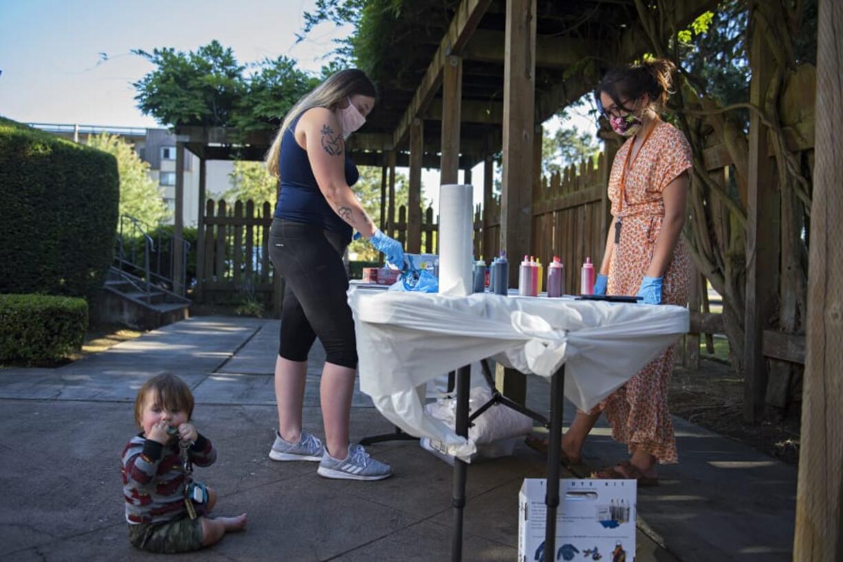 Carter Campbell, 8 months, from left, joins his mom, Breeanna Campbell, as she creates a colorful tie-dye shirt with the help of Julie Tappan, independent living skills resource specialist, at the YWCA on Tuesday evening. The summer celebration was for young people who are participating in YWCA Clark County&#039;s Independent Living Skills program. These youth have all aged out of the foster care system and are learning to live on their own.