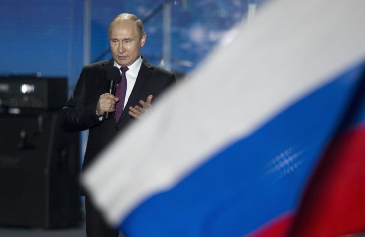 FILE - In this file photo dated Wednesday, March 14, 2018, Russian President Vladimir Putin speaks in front of a Russian National flag in Sevastopol, Crimea.  An influential committee of British lawmakers plans to publish its findings Tuesday July 21, 2020, reporting on Russian interference in British politics, amid criticism the government delayed its release for more than six months to shield Prime Minister Boris Johnson and his Conservative Party from embarrassment.