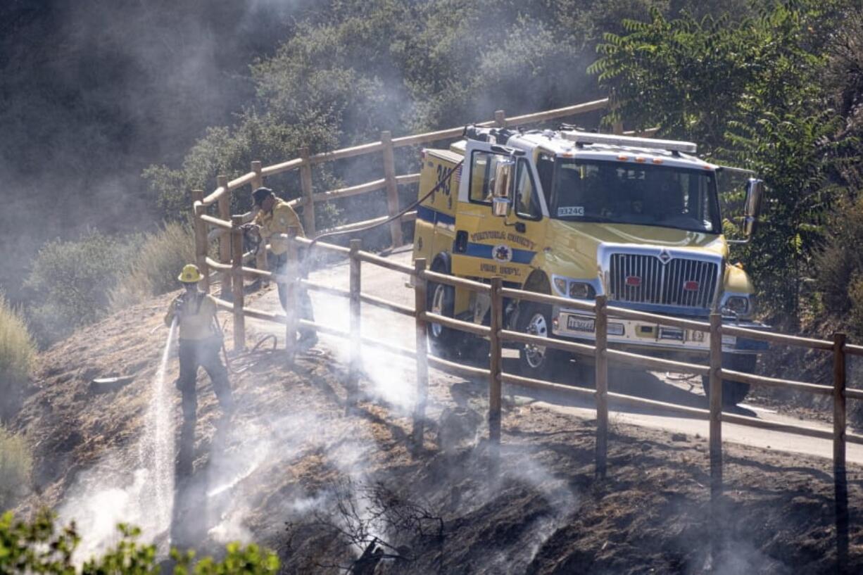 FILE - In this Monday, July 6, 2020 file photo, firefighters douse hot spots along Agua Dulce Canyon road in Agua Dulce, Calif. Emergency personnel are working through high temperatures to contain the Soledad fire in Southern California. In early July 2020, meteorologists say temperatures will be stuck with above normal temperatures through the month if not longer.