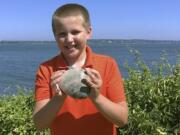 In this Tuesday, July, 28, 2020, photo provided by the University of Rhode Island, Cooper Monaco holds the large quahog he found Monday while clamming with his grandfather in Westerly, R.I. The quahog is more than five inches across and weighing more than two pounds, and is among the largest ever harvested in the state. The mollusk was donated to the University of Rhode Island&#039;s Marine Science Research Facility.