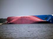 FILE - In this Sept. 9, 2019, file photo, a Moran tugboat nears the stern of the capsizing vessel Golden Ray near St. Simons Sound off the coast of Georgia. The salvage team salvage team is seeking a federal permit to surround the shipwreck with a giant mesh barrier to contain any debris when they cut the ship apart. (AP Photo/Stephen B.