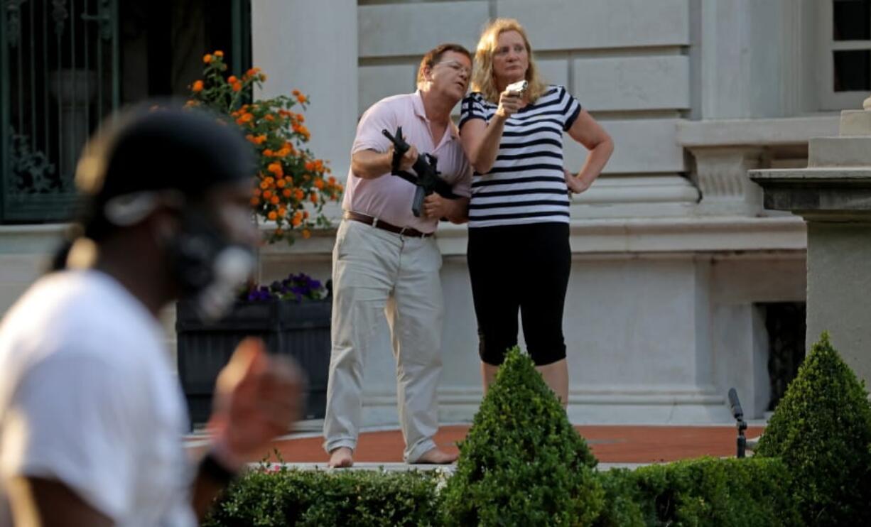 FILE - In this June 28, 2020 file photo, armed homeowners Mark and Patricia McCloskey, standing in front their house along Portland Place confront protesters marching to St. Louis Mayor Lyda Krewson&#039;s house in the Central West End of St. Louis. An affidavit in a court case shows that the white St. Louis couple who stood outside their mansion with guns during a protest have pulled a gun before. Mark McCloskey says in the affidavit that they pointed a gun at a neighbor once as a warning to stay off their property. They claim they own a small piece of land, while trustees of their private street say they own it. (Laurie Skrivan/St.