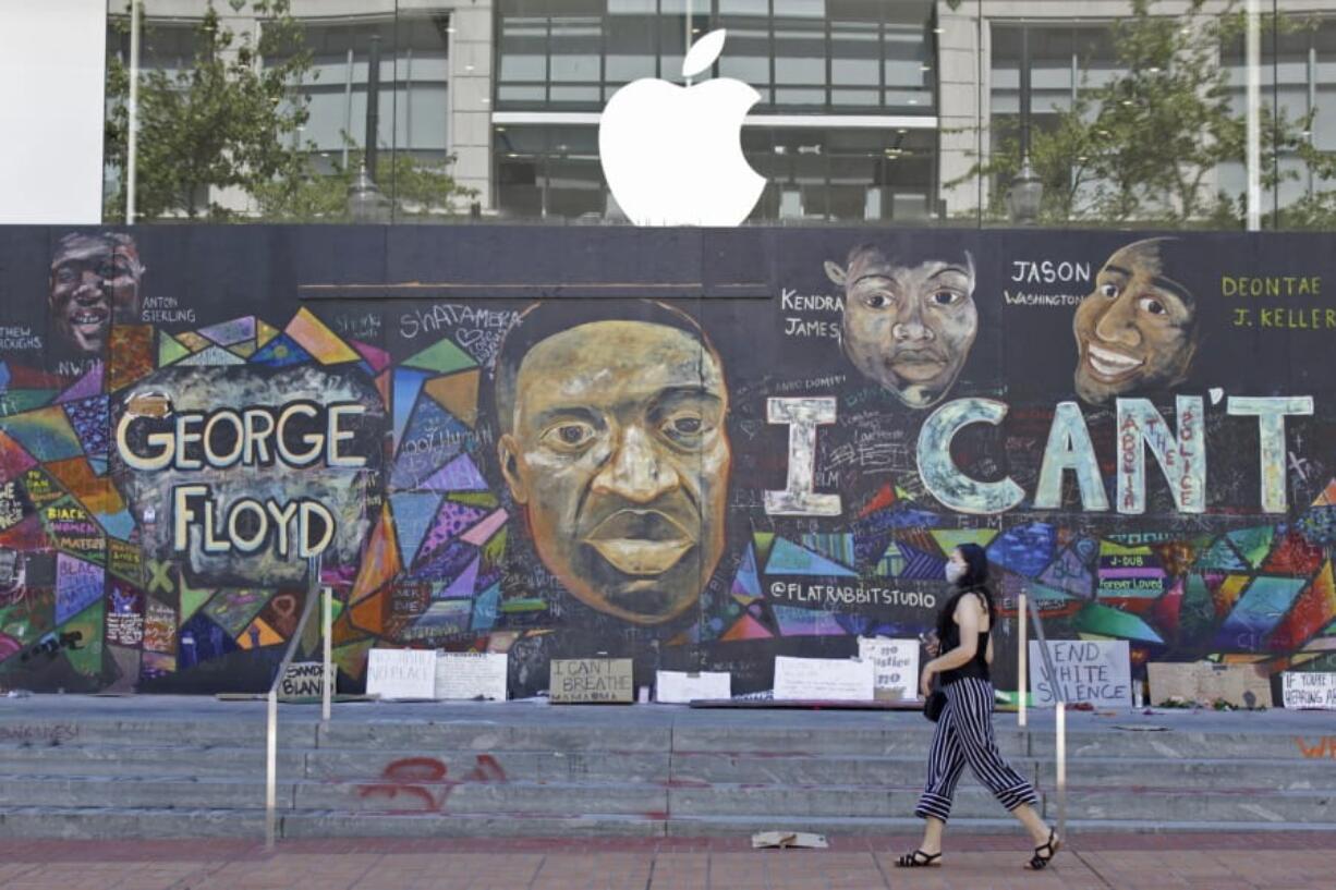 A pedestrian walks past a boarded-up Apple store that&#039;s been covered in street art in downtown Portland, Ore., Monday, July 13, 2020. While most demonstrations in the city have been peaceful, nightly violent clashes between police and protesters have divided Portland, paralyzed the downtown and attracted the attention of President Donald Trump, who sent federal law enforcement to the city to quell the unrest.