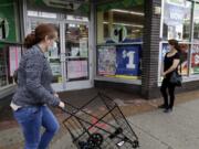 FILE - In this Friday, May 15, 2020, file photo, a woman wearing a mask, left, walks by a Dollar Tree, while another woman waits in line to shop at the store, which is limiting customers amid the coronavirus pandemic, in Chicago. (AP Photo/Nam Y.