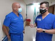 FILE - In this July 16, 2020 file photo, Infectious Disease Physician Army Maj. Gadiel Alvarado, right, with the Urban Augmentation Medical Task Force, talks with United Memorial Medical Center&#039;s Dr. Joseph Varon, inside a newly setup hospital wing in Houston. Texas reported a new daily record for virus deaths Friday and more than 10,000 confirmed cases for the fourth consecutive day. (AP Photo/David J.