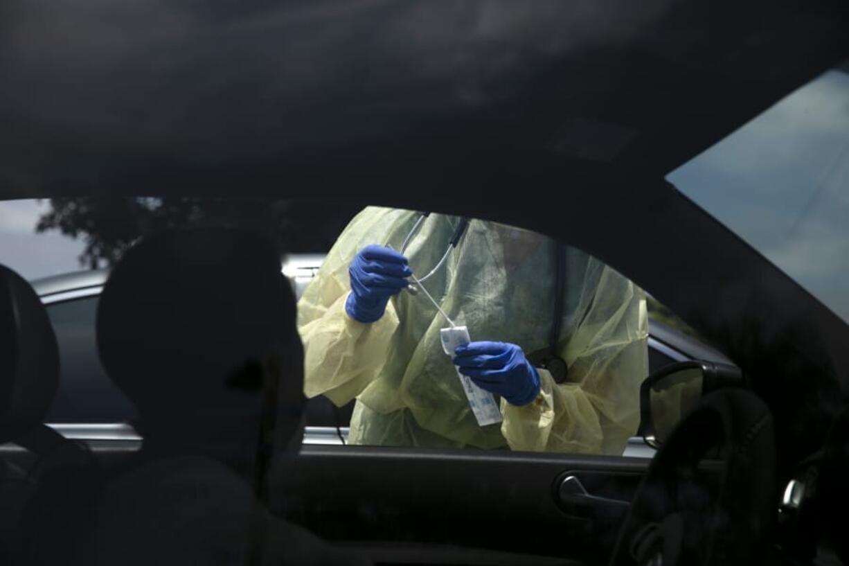 A physician assistant prepares to collect a nasal swab sample from a patient for COVID-19 testing. (AP Photo/Jae C.