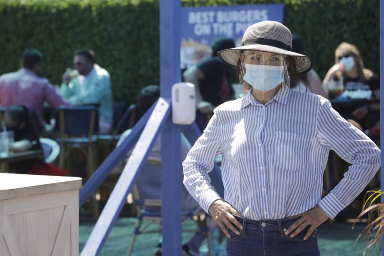 A hostess waits to sit customers on a restaurant at the pier Sunday, July 12, 2020, in Santa Monica, Calif., amid the coronavirus pandemic. A heat wave has brought crowds to California&#039;s beaches as the state grappled with a spike in coronavirus infections and hospitalizations.