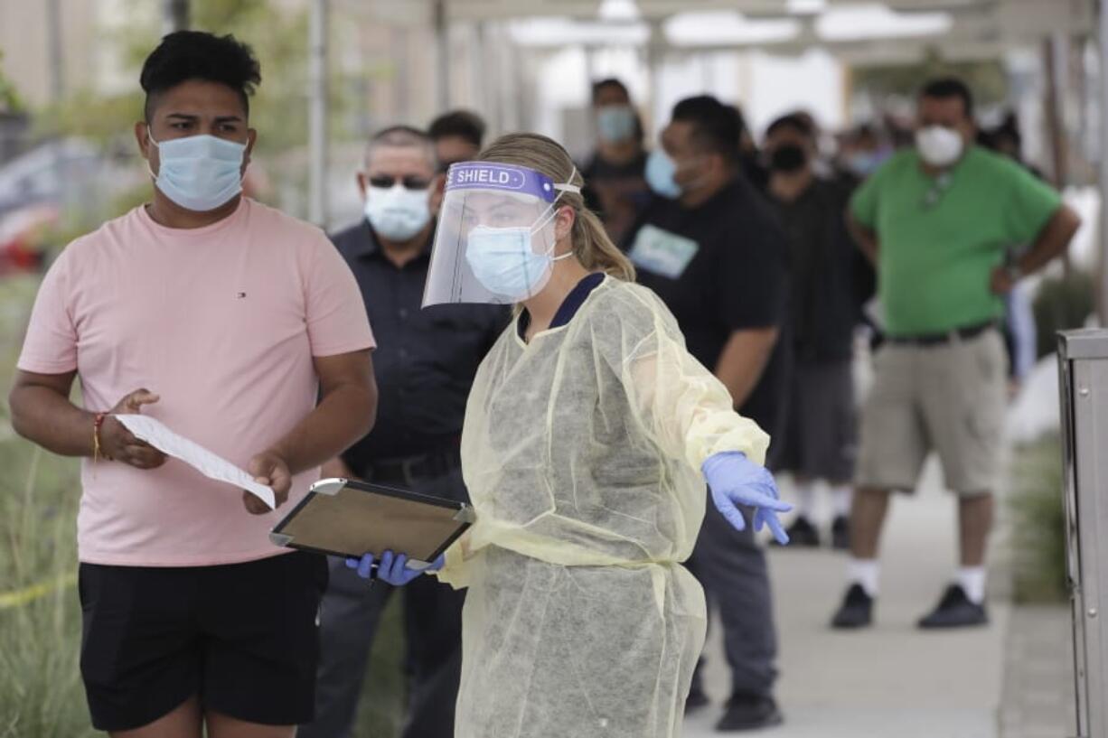 FILE - In this July 22, 2020, file photo, people line up behind a health care worker at a mobile Coronavirus testing site at the Charles Drew University of Medicine and Science, in Los Angeles. As the world races to find a vaccine and a cure for COVID-19, there is seemingly no antidote in sight to the burgeoning outbreak of coronavirus conspiracy theories, hoaxes, anti-mask myths and sham treatments.