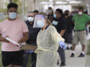 FILE - In this July 22, 2020, file photo, people line up behind a health care worker at a mobile Coronavirus testing site at the Charles Drew University of Medicine and Science, in Los Angeles. As the world races to find a vaccine and a cure for COVID-19, there is seemingly no antidote in sight to the burgeoning outbreak of coronavirus conspiracy theories, hoaxes, anti-mask myths and sham treatments.