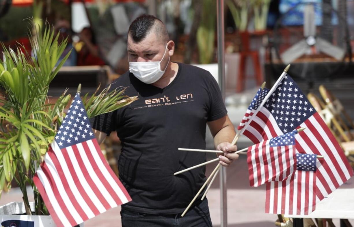 Marvin Turcios puts out American flags at Ocean&#039;s 10 restaurant on Miami Beach, Florida&#039;s famed Ocean Drive on South Beach, July 4, 2020. The Fourth of July holiday weekend began Saturday with some sobering numbers in the Sunshine State: Florida logged a record number of people testing positive for the coronavirus.