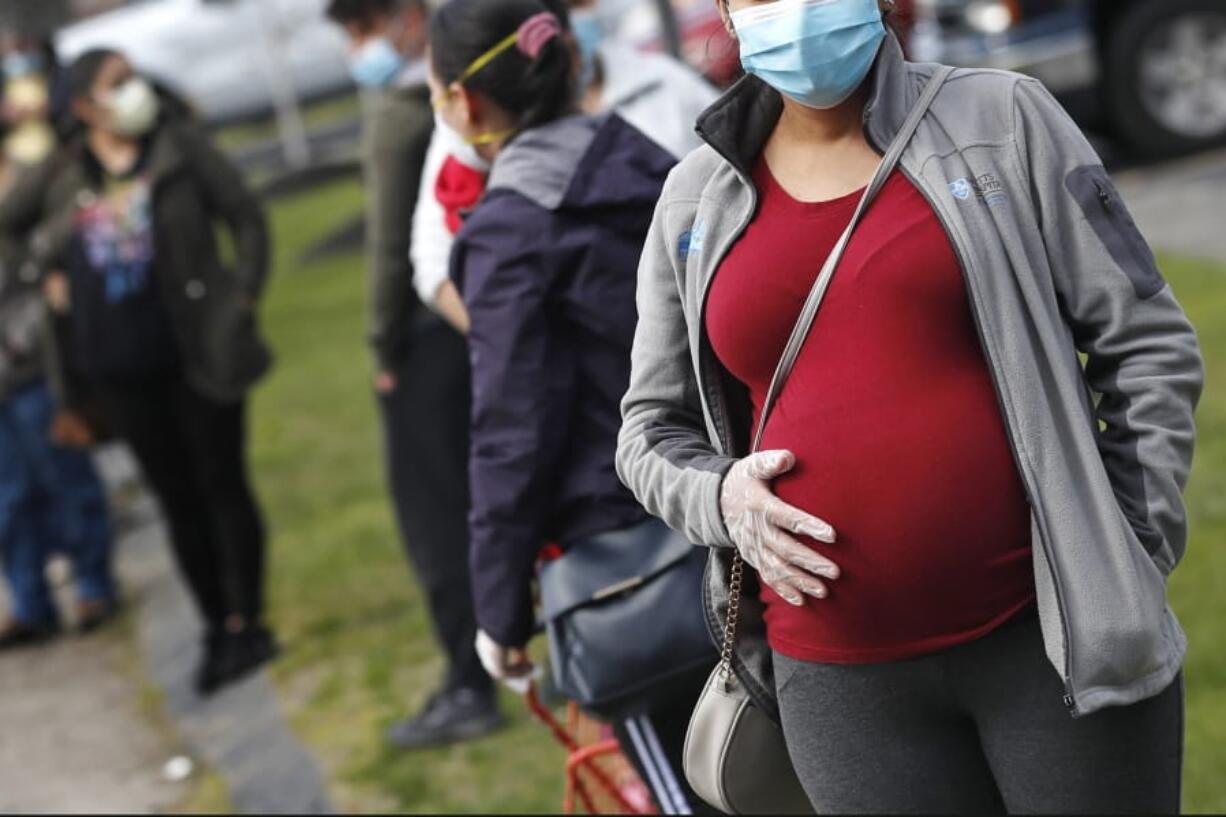 FILE - In this Thursday, May 7, 2020 file photo, a pregnant woman wearing a face mask and gloves holds her belly as she waits in line for groceries with hundreds during a food pantry sponsored by Healthy Waltham for those in need due to the COVID-19 virus outbreak, at St. Mary&#039;s Church in Waltham, Mass. A small study in Italy strengthens evidence that pregnant women infected with the coronavirus might be able to spread it to a fetus before birth. Research was released on Thursday, July 9, 2020.