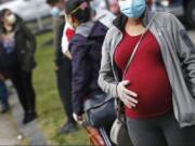 FILE - In this Thursday, May 7, 2020 file photo, a pregnant woman wearing a face mask and gloves holds her belly as she waits in line for groceries with hundreds during a food pantry sponsored by Healthy Waltham for those in need due to the COVID-19 virus outbreak, at St. Mary&#039;s Church in Waltham, Mass. A small study in Italy strengthens evidence that pregnant women infected with the coronavirus might be able to spread it to a fetus before birth. Research was released on Thursday, July 9, 2020.