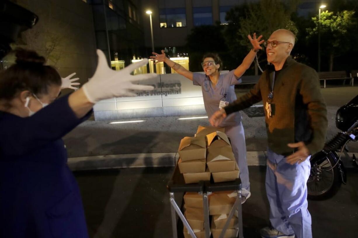 Nightbird Restaurant chef and owner Kim Alter, left, mimics giving a hug to nurse practitioner Sydney Gressel, center, and patient care technician Matt Phillips on March 27 after delivering dinner to them at University of California at San Francisco Benioff Children&#039;s Hospital in San Francisco.